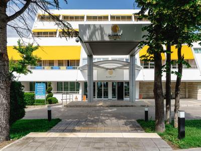 Modernes Hotelgebäude mit gelben Akzenten und Eingang mit Überdachung, von Bäumen umgeben