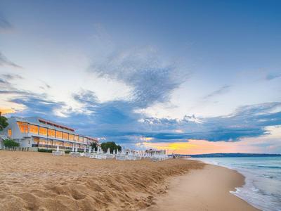 Zandstrand met hotelgebouw, ligstoelen en blauwe lucht bij zonsondergang