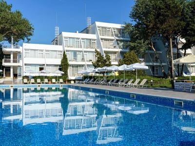 Modern hotelcomplex met zwembad, ligstoelen en parasols onder een blauwe lucht
