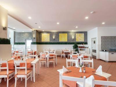 Licht, modern restaurant met oranje gedekte tafels en witte stoelen.