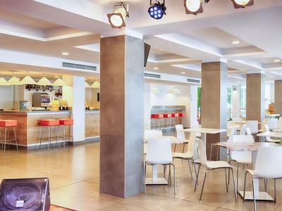 Helle, moderne Hotel-Lounge mit weißen Stühlen, Holzböden und Barbereich im Hintergrund.