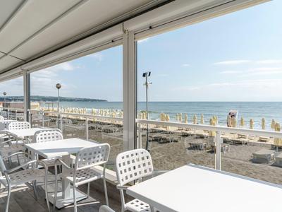 Überdachte Terrasse mit weißen Tischen und Stühlen mit Blick auf den Strand und das Meer.