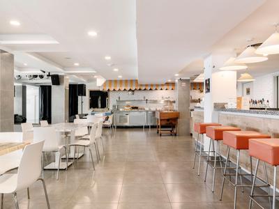 Heller Speisesaal mit weißen Stühlen und einer Bar mit orangen Hockern.