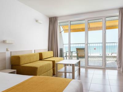 Modern hotelkamer met gele bank en grote glazen wand met uitzicht op zee.