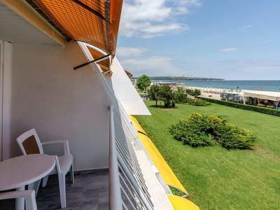Balkon met stoelen en tafel met uitzicht op een grasgebied en de zee bij helder weer.