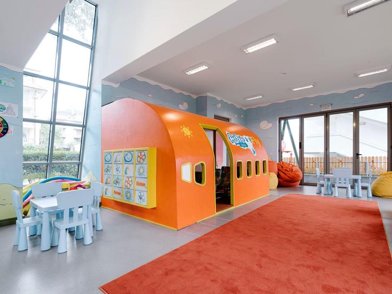 Lichte speelruimte voor kinderen met oranje speelhuis en knutseltafel in lichte kamer met grote ramen.