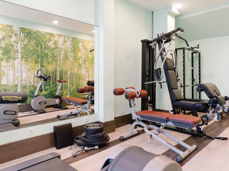 Heldere fitnessruimte met gewichten, loopband, hometrainer en krachtmachine voor grote spiegel.