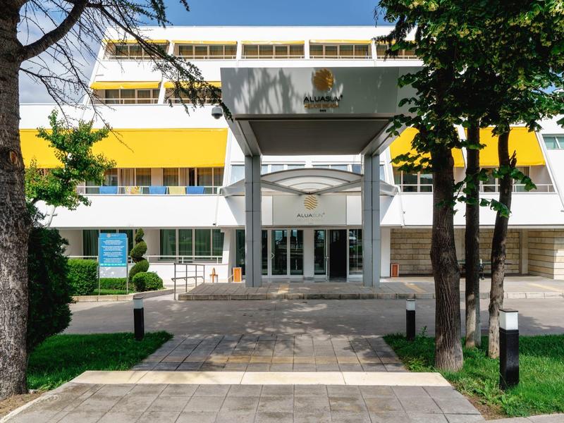 Ingang van een modern hotel met gele accenten en bomen op de voorgrond.