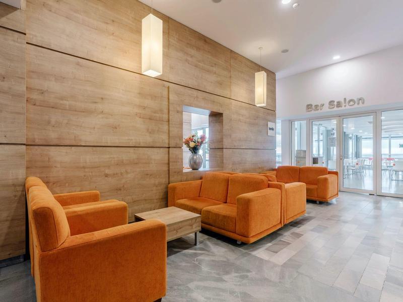 Moderne hotel-loungesfeer met oranje fauteuils en houten wandbekleding.