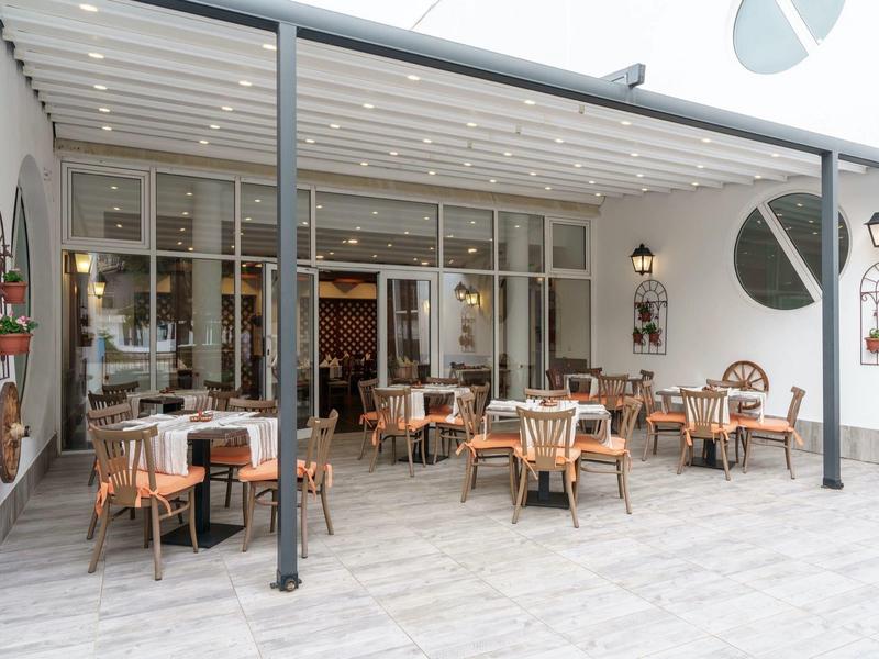Moderne buitenruimte van een hotel met tafels en stoelen onder een zonnescherm.