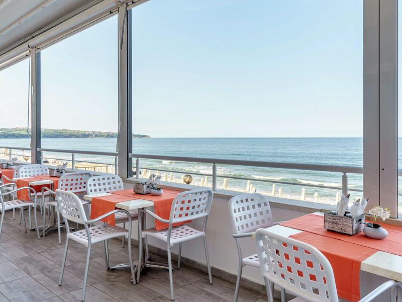 Terras met oranje gedekte tafels en witte stoelen met uitzicht op zee.