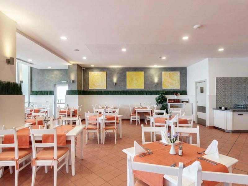 Licht, modern restaurant met oranje gedekte tafels en witte stoelen.