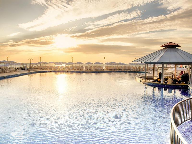 Groot buitenzwembad met paviljoenbar en zonsondergang aan de hemel.