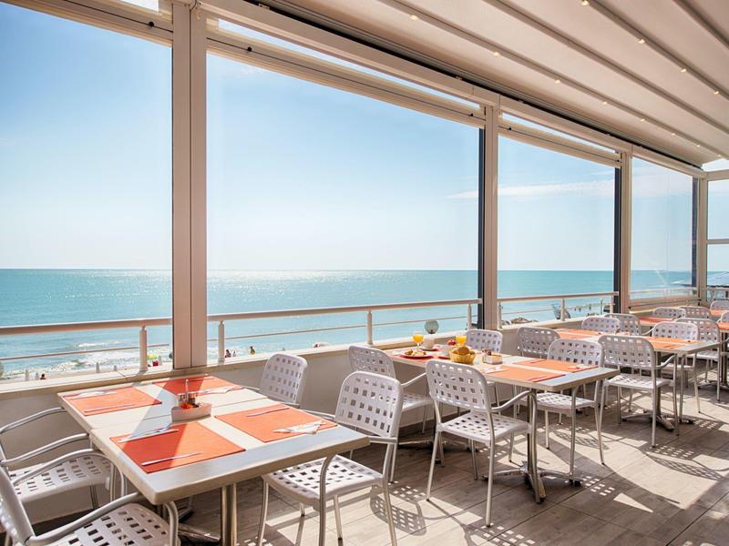 Terras met tafels en stoelen met uitzicht op zee bij heldere hemel.