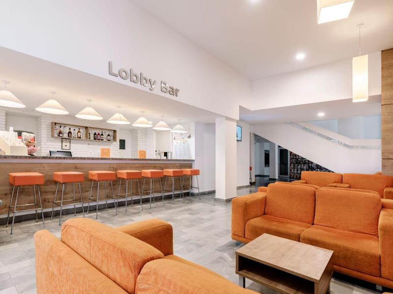 Moderne hotel lobby met oranje banken en een bar met krukken.