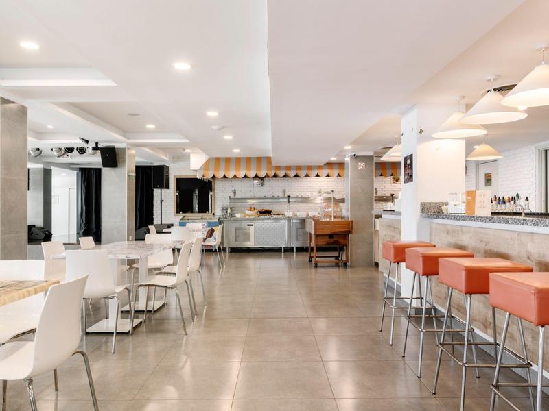 Lichte, moderne eetruimte met witte stoelen, oranje barkrukken en open keuken.