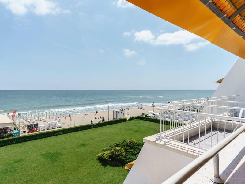 Uitzicht vanaf een balkon op groen grasveld en zandstrand aan zee.