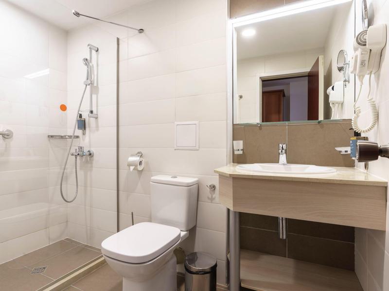 Moderne hotelbadkamer met inloopdouche, toilet en verlichte spiegel.