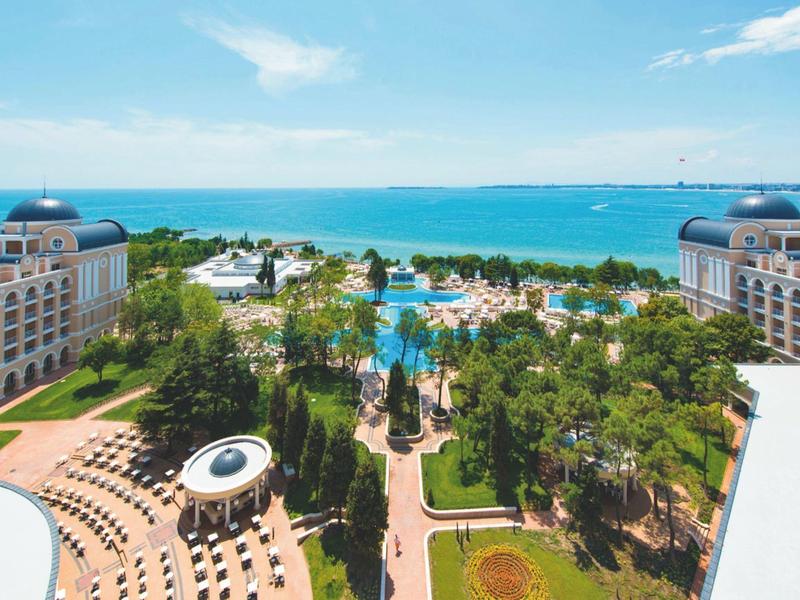 Luxury hotel with pool, gardens, and sea view under a blue sky.