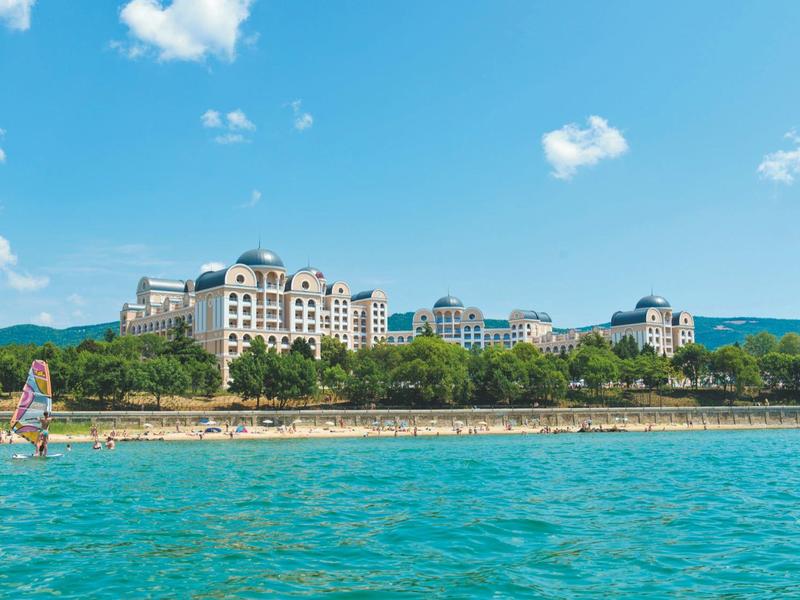 Woman walks on beach with hotel building and blue sky in background.