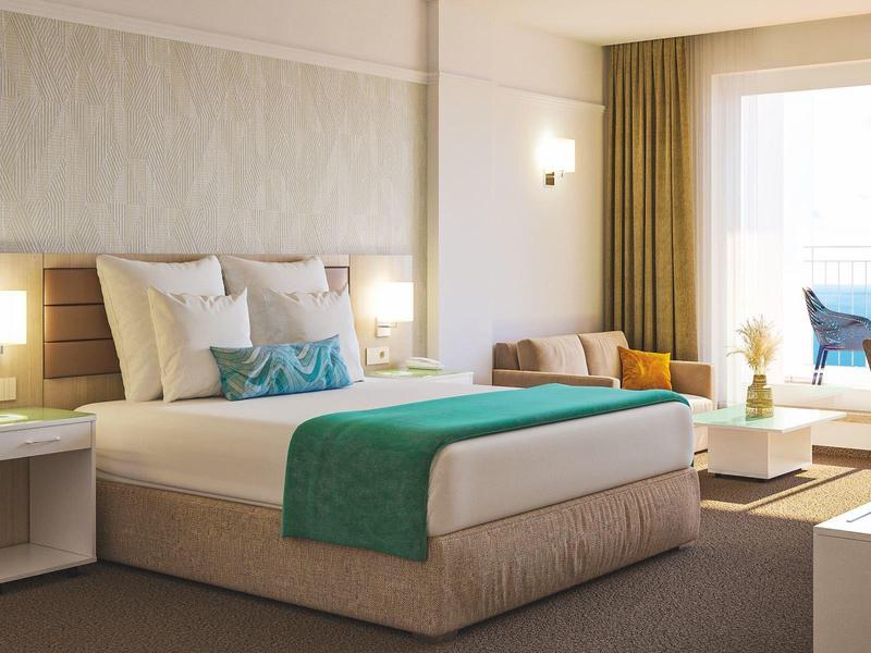 Modern hotel room with large bed, white pillows, turquoise accents, bright and inviting.