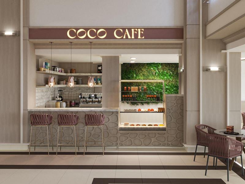 Modern, elegant café area with counter, seating, and green plant backdrop.