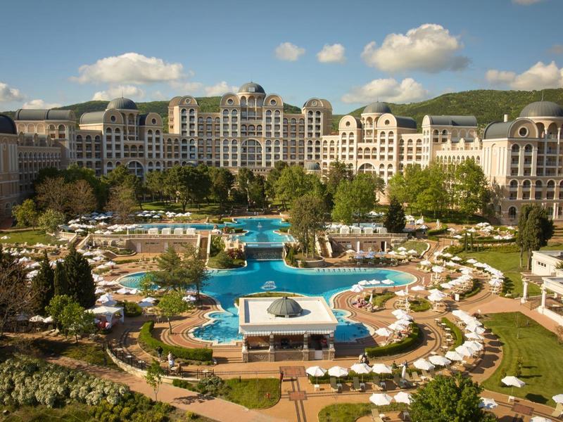Large luxury hotel with multiple pools and numerous sun loungers under a blue sky
