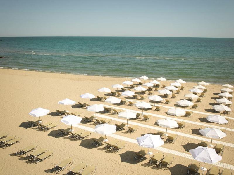 Empty sunbeds with white umbrellas on a calm beach under clear sky.