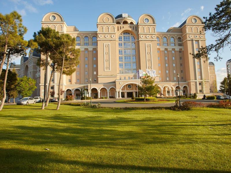 Large beige hotel building with towers, surrounded by trees and a well-kept lawn.