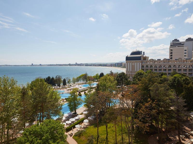 Luxury hotel with pool area next to a large lake under a blue sky.