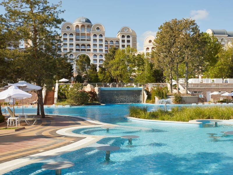Hotel with outdoor pool, sun loungers, and umbrellas in a sunny garden setting.