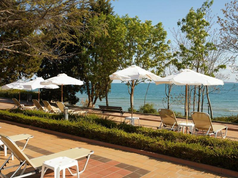 Beach with loungers and umbrellas surrounded by trees, overlooking the sea.