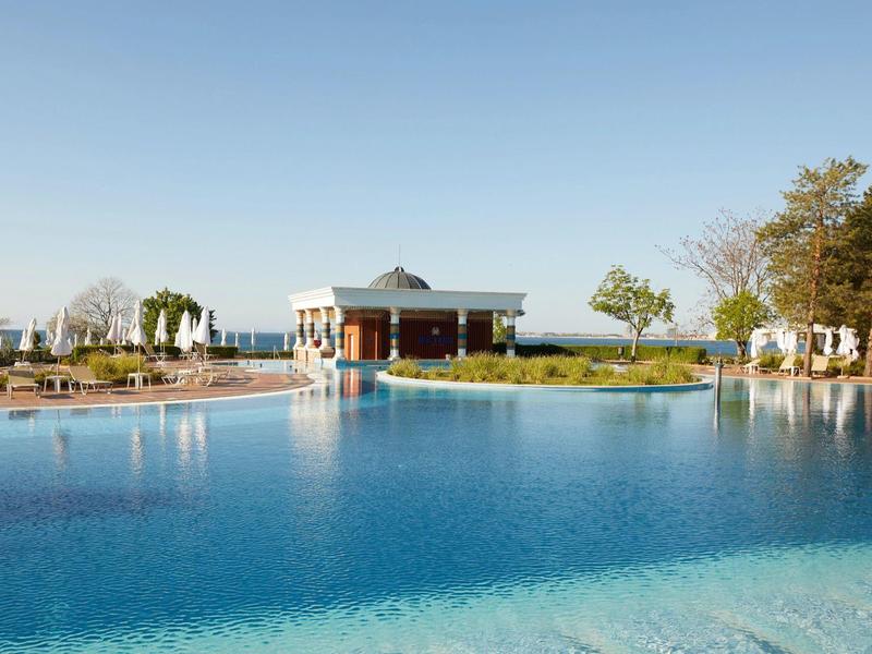 Large outdoor hotel pool with surrounding lounge chairs and umbrellas on a sunny day.