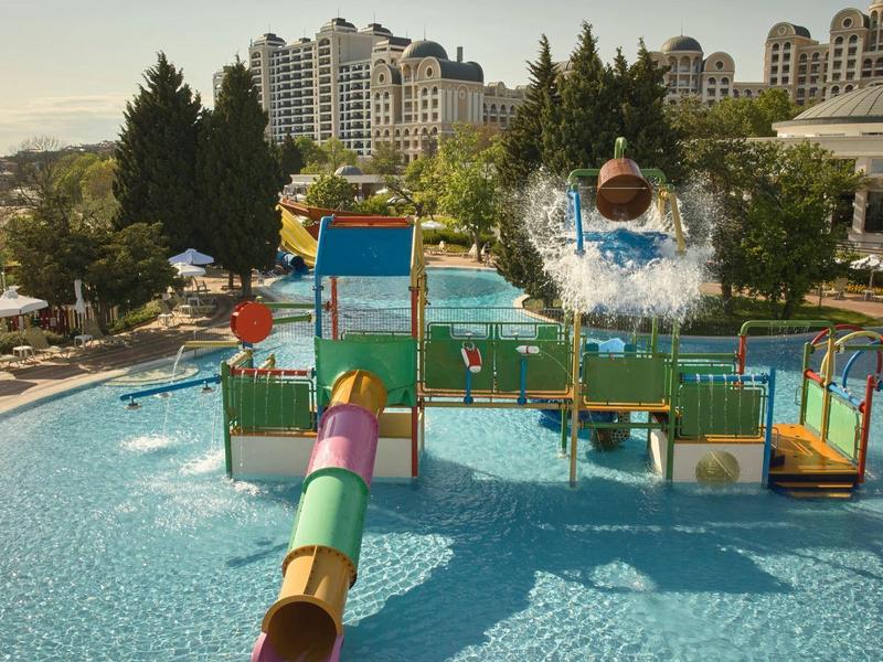 Colorful water playground in pool with hotel buildings in the background on sunny day.