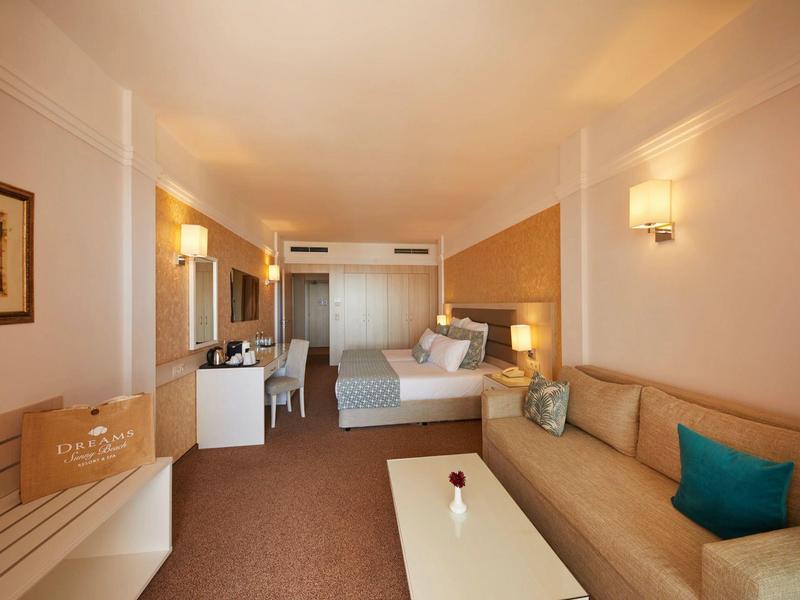 Modern hotel room with sofa, bed, desk, and warm lighting.