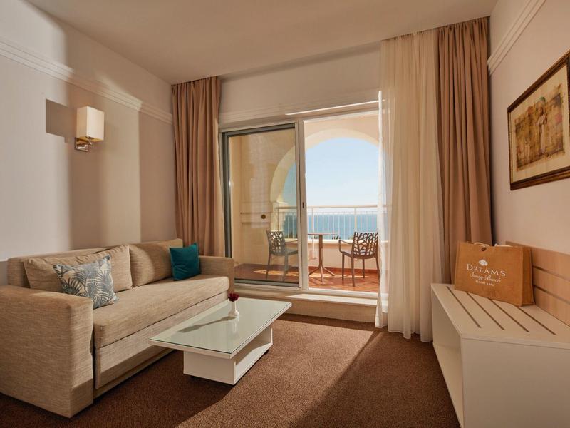 Bright hotel room with sofa, coffee table, and balcony overlooking the sea.