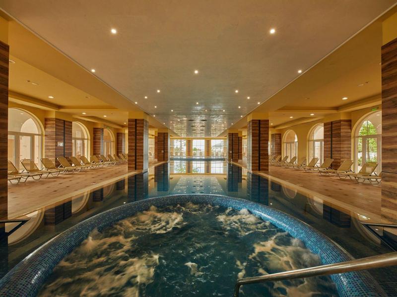 Luxurious indoor pool with hot tub, relaxing loungers, and large panoramic window.