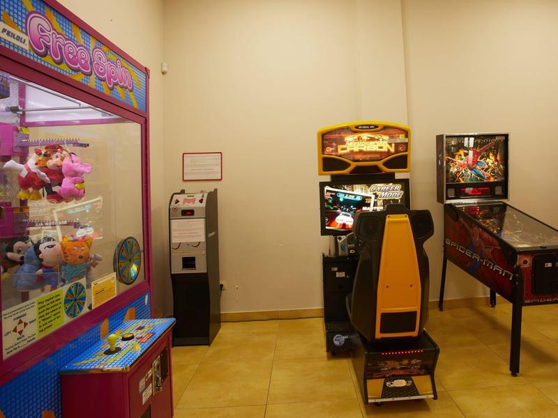 Arcade machines and a phone stand in a simple, yellow-lit room.