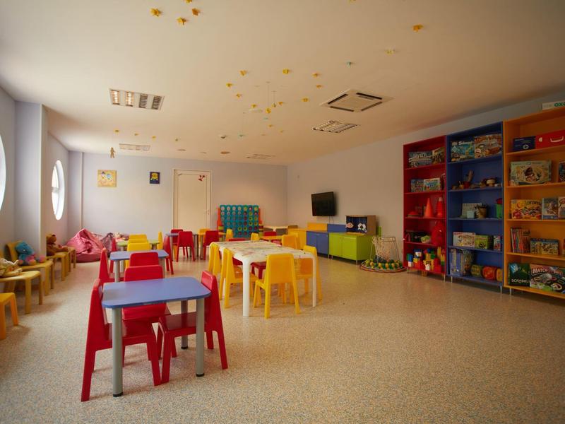 Bright, colorful children's playroom with small tables, chairs, and toy shelves.