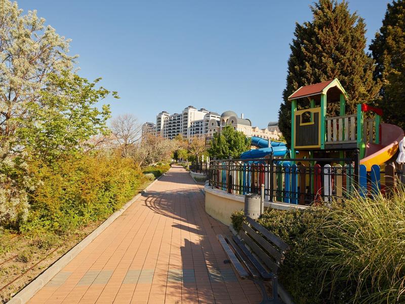 A quiet paved path with a playground and trees on a sunny day.