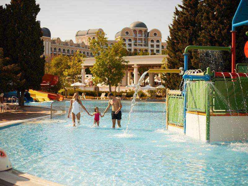 Family with two children walks through a hotel pool with play area.