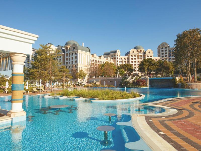 Luxurious hotel with large pool and surrounding trees on a sunny day.