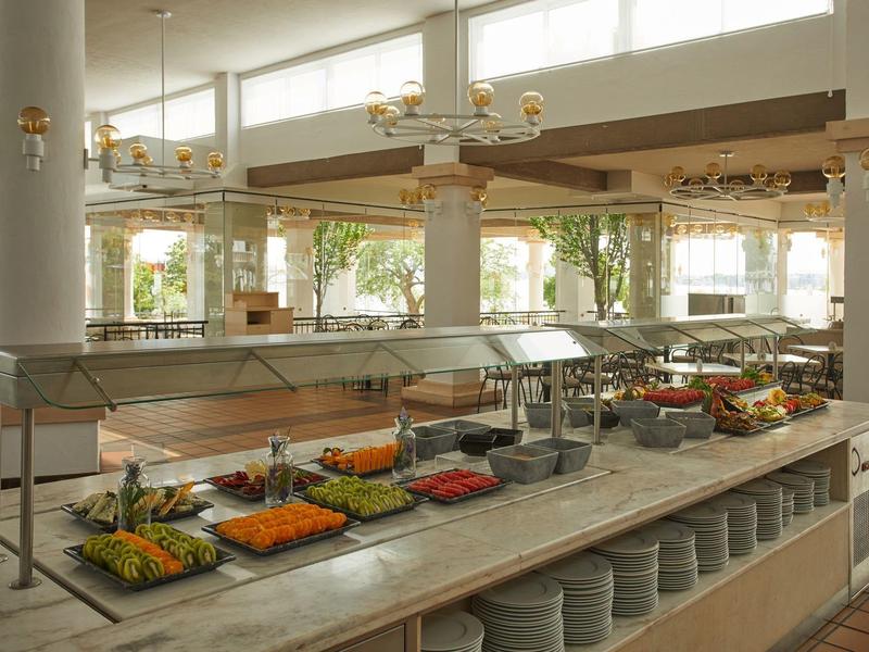 Buffet area with fresh vegetables, fruit, and dishes in a bright, open space with large windows.