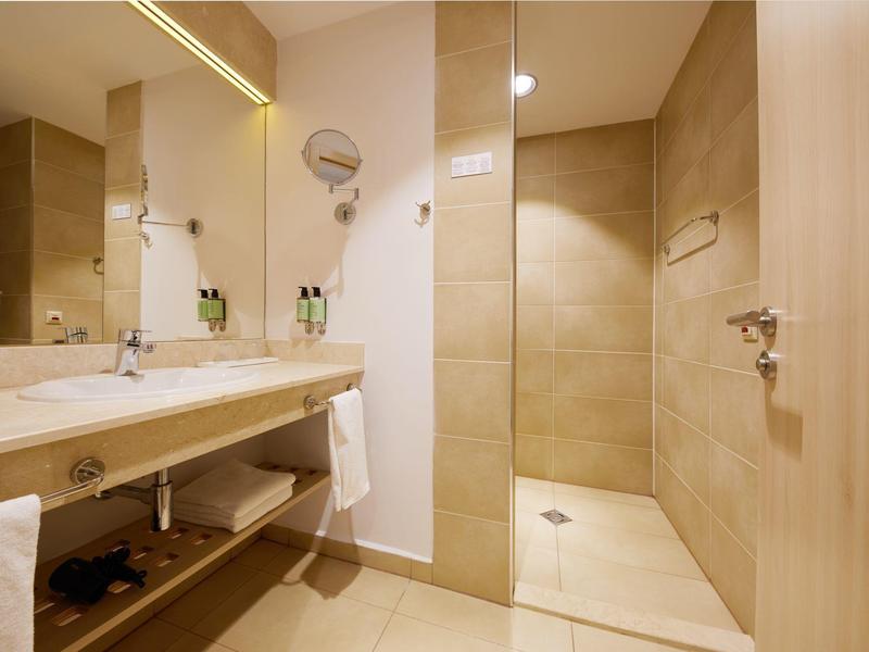 Bright bathroom with large mirror wall and open shower in neutral beige tones.