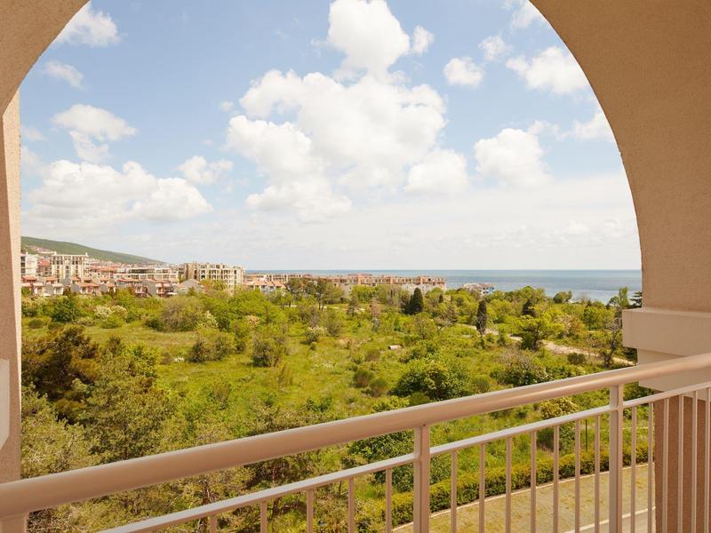 View from a balcony with railing over green landscape and sea on the horizon