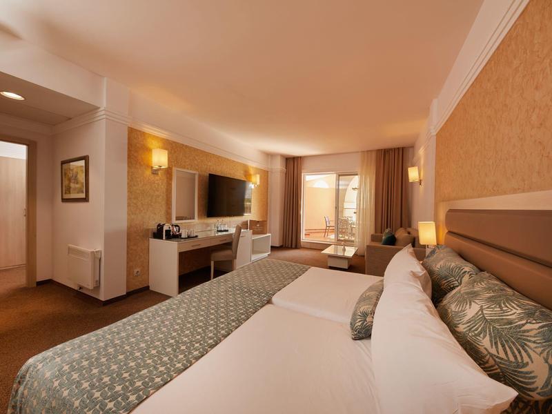 Bright hotel room with double bed, TV, desk, and window view.