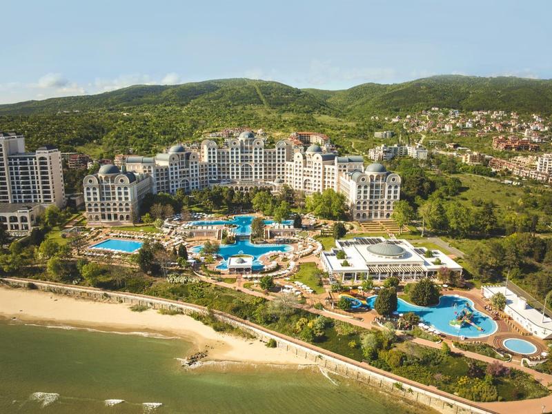 Luxury resort with multiple pools by the beach and green hills in the background.