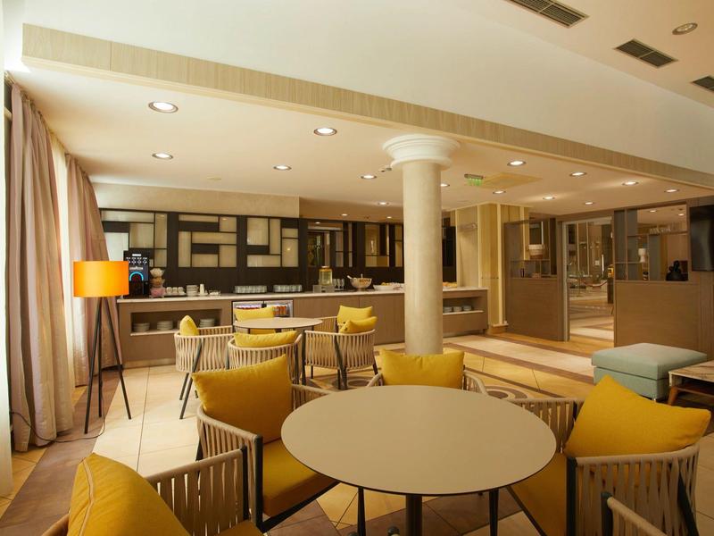 Bright modern hotel room with dining area and cozy seating in warm colors.