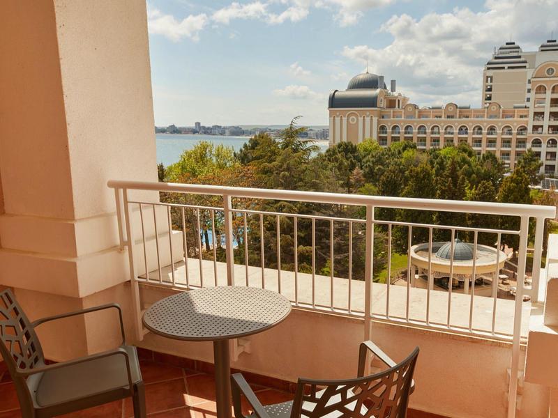 Balcony with table and chairs, view of water and hotel building in the background.