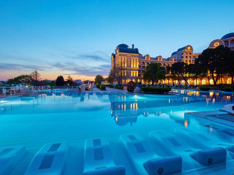 Large hotel pool at dusk with illuminated building in the background